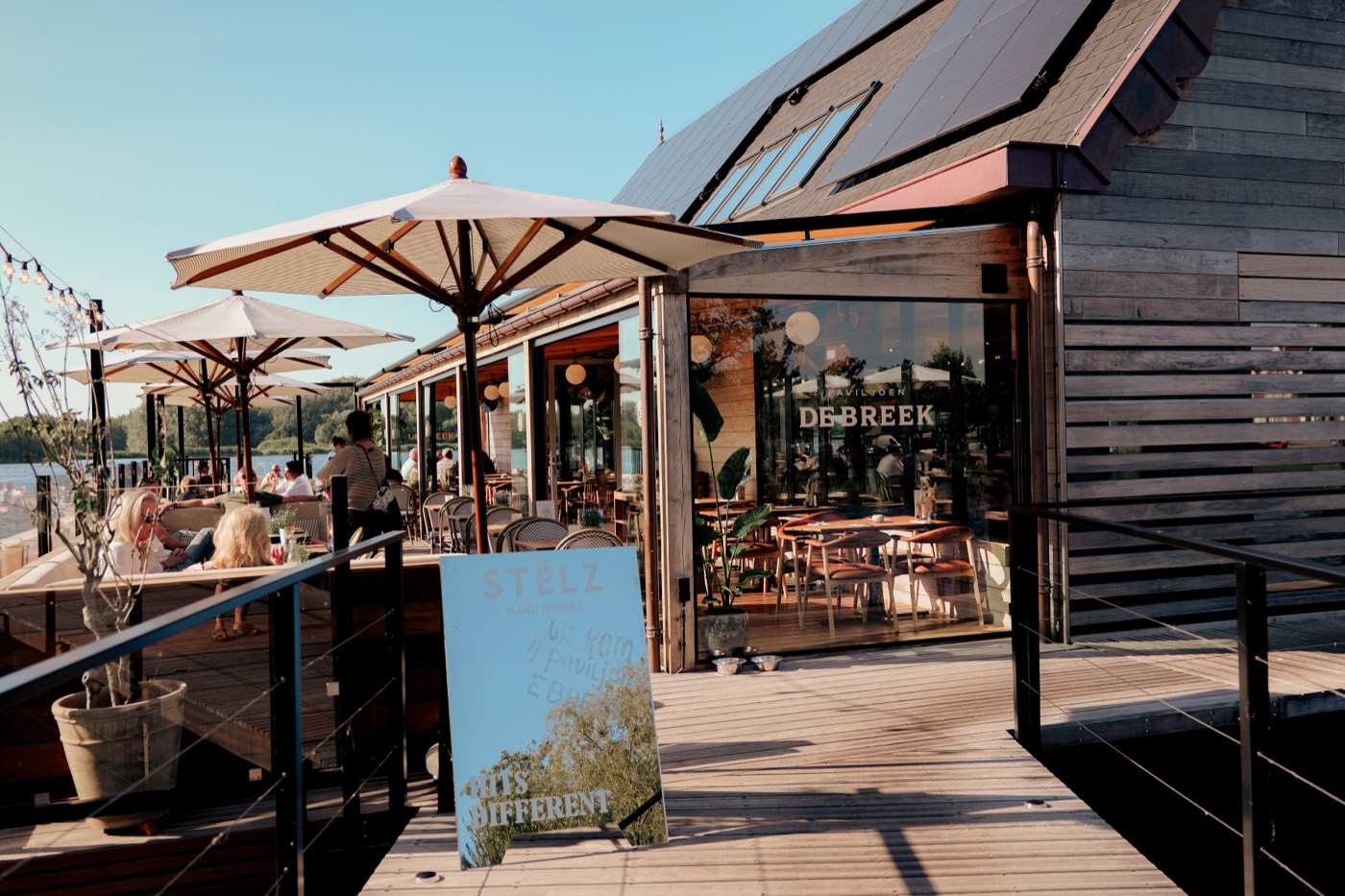 Terras van Paviljoen De Breek vol gasten bij zonsondergang